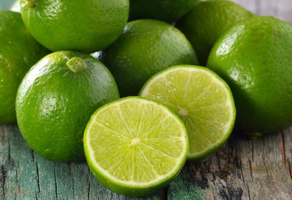 Citron vert frais découpés et entiers présentés sur une table en bois